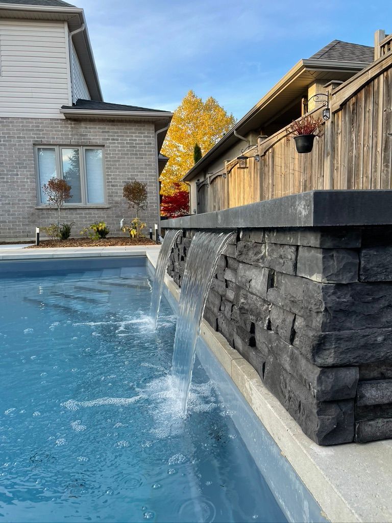 Pool with sheer-descent waterfall over charcoal stone wall